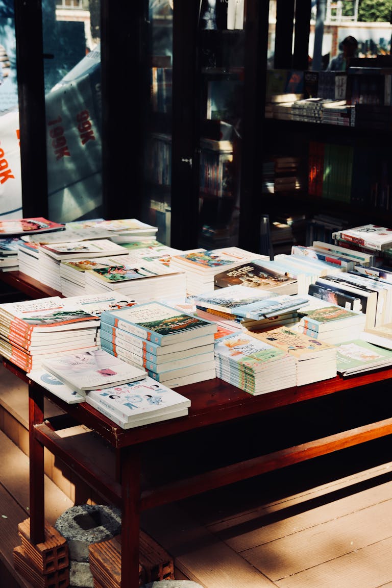 A sunlit table in a bookstore with various stacked books on display.